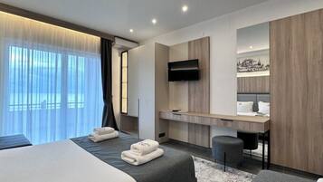 A modern hotel room with two beds, a desk, a TV, and a cityscape view.