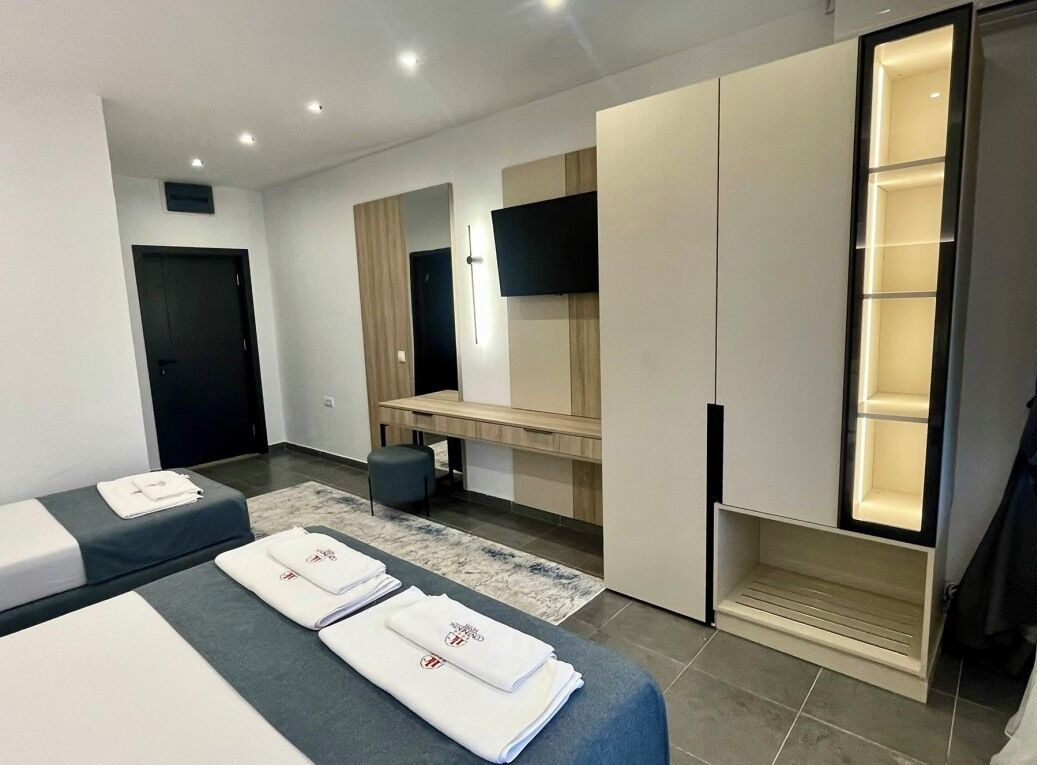 A modern hotel room with two beds, a flat-screen TV, a wardrobe, and a built-in shelf.