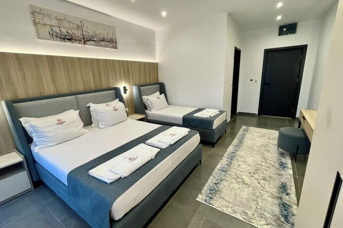 A modern hotel room with two beds, a large rug, and a cityscape painting on the wall.