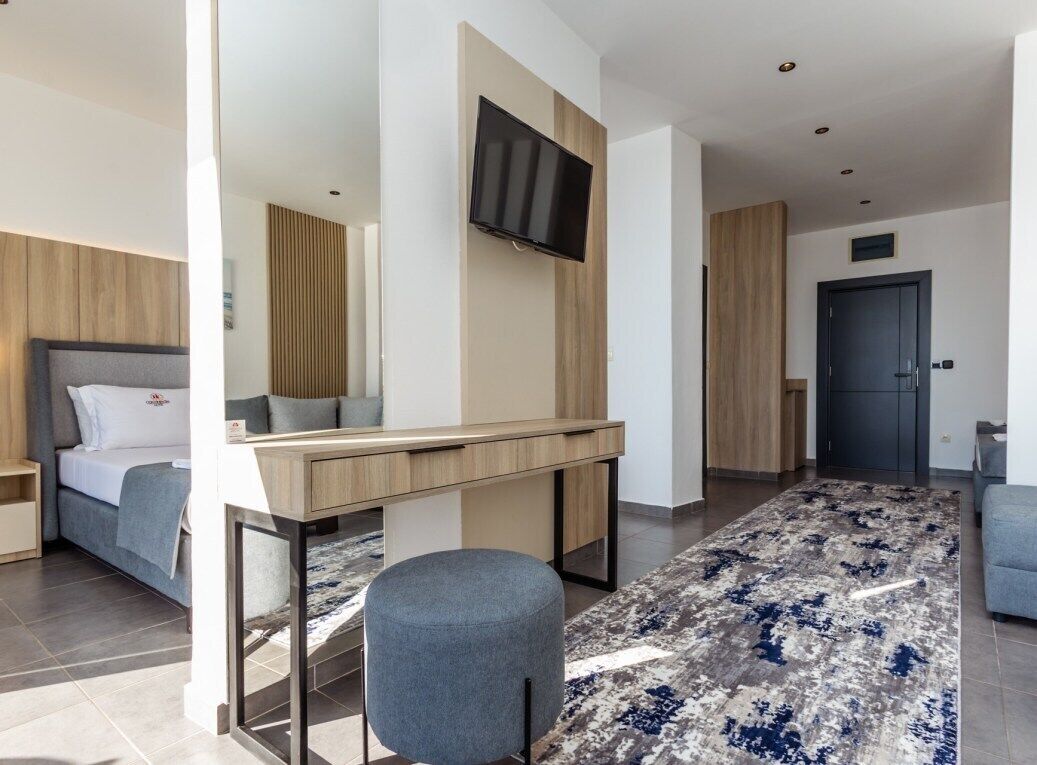Ein modernes Hotelzimmer mit Bett, Schreibtisch, Stuhl, Wand-Fernseher und einem gemusterten Teppich.