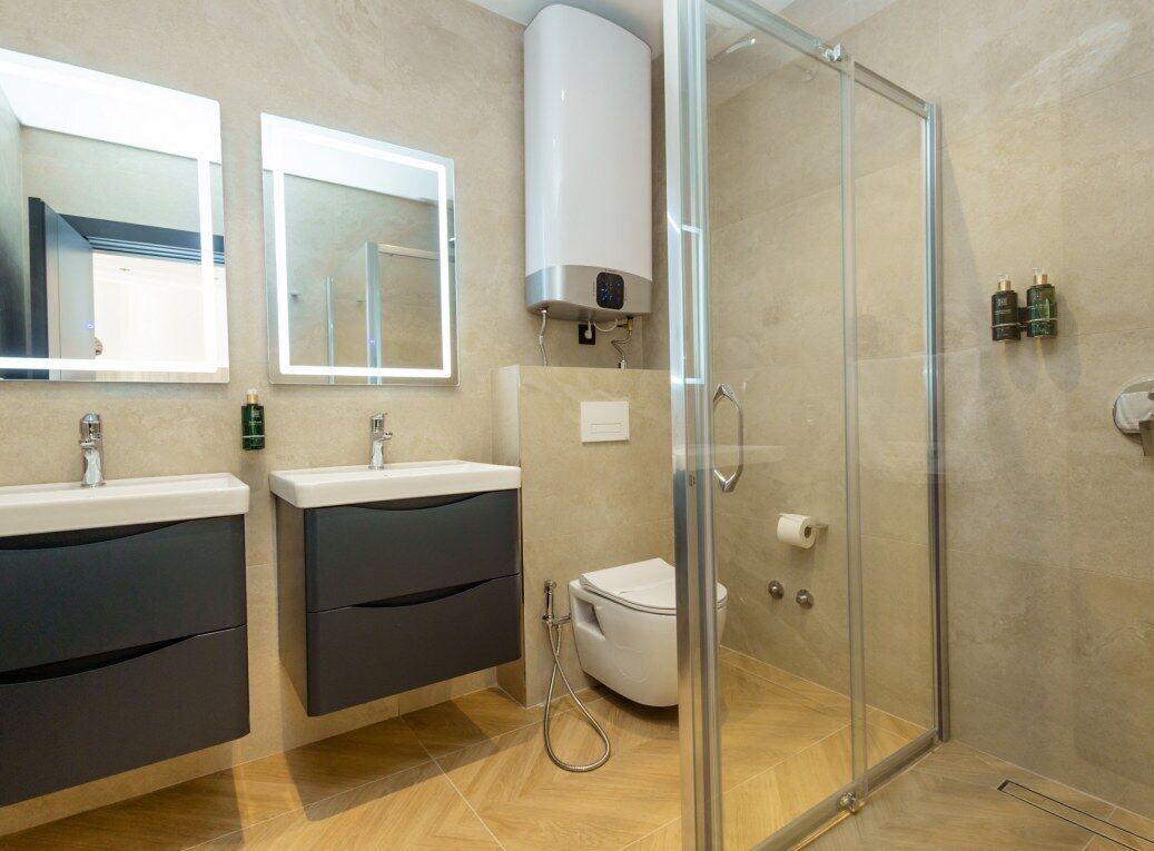 Et moderne badeværelse med to håndvaske, toilet, brusekabine i glas og indbygget varmelegeme.