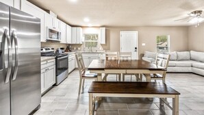 Una cucina moderna con elettrodomestici in acciaio inossidabile, un tavolo da pranzo con sedie e un divano chiaro in un ampio soggiorno.