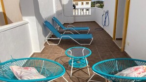 A balcony with two blue lounge chairs and a small round table, white walls, and a view of buildings in the background. - Cozy townhouse in Vera, just steps from the beach (vera)