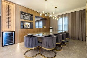 A modern dining area with a glass-top table, grey upholstered bar stools, and a chandelier.