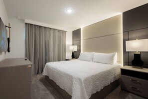 A hotel room with a large bed, two bedside tables with lamps, a desk, and a guitar on the wall.