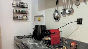 A compact kitchen with a gas stove, a coffee maker, and a microwave. There are shelves with jars and a hanging rack with utensils. - Modern apartment in the heart of Marrakech, 9 min from airport -with Wi-Fi & A/C (Marrakech)