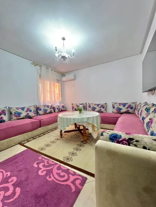 A living room with a sofa set, a round coffee table, a chandelier, and a patterned rug.