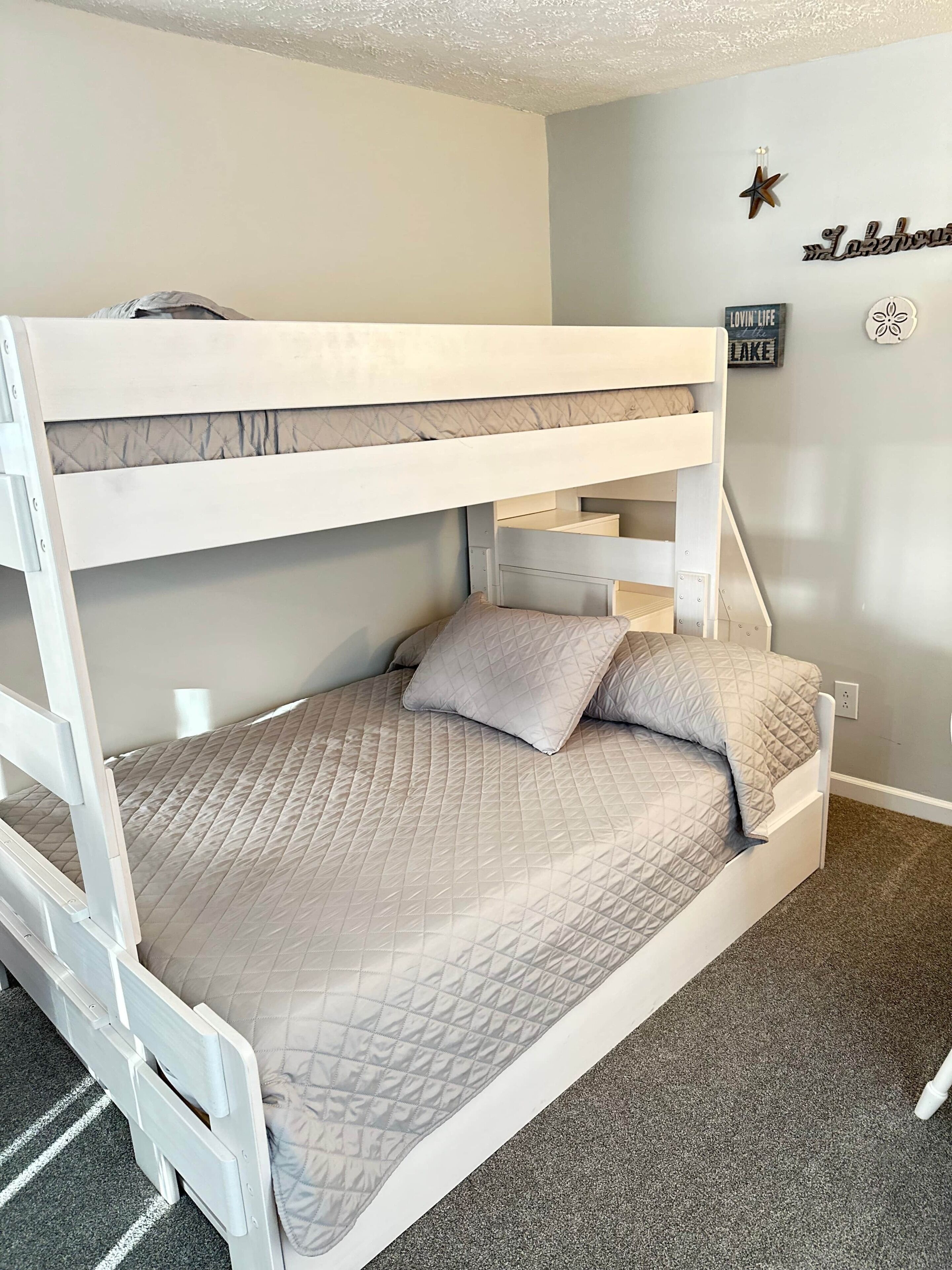 A bunk bed with a quilted mattress, a ladder, and a wall with a star decoration and a sign.
