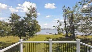 A deck with a railing overlooking a grassy area with trees and a body of water. - Otsego Lake Escape, Sleeps 14, Skiing, Snow trails, Fire Pit (Bagley Township)
