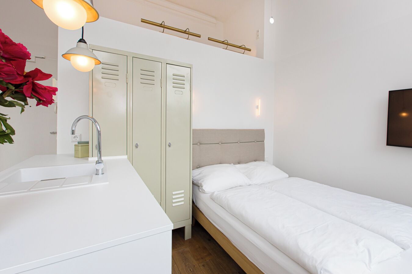 A bedroom with a single bed, a white dresser with a sink, and a set of lockers.