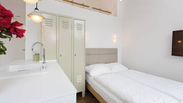 A bedroom with a single bed, a white dresser with a sink, and a set of lockers.