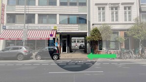 Straßenansicht eines Gebäudes mit einer Ladenfront, einem roten und weißen Streifenmarkisenvorzelt, einem Schild mit verschiedenen Firmennamen und einem Fahrradstellplatz.