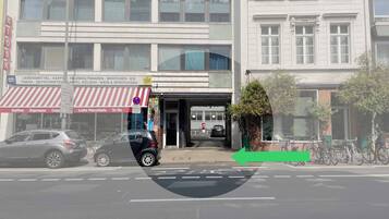 A street view with a building featuring a storefront with a red and white striped awning, a signboard with various business names, and a bicycle parking area.