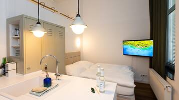 A hotel room with a bed, a TV, a bathroom with a sink and mirror, and a window with blinds.