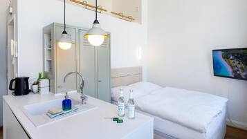 A hotel room with a white sink, mirror, and bed. There are two bottles of hand sanitizer on the sink.