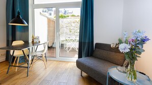 A room with a dining table, chairs, a sofa, a small table with a vase of flowers, and a hanging lamp. - Sunny, quiet city apartment with sleeping gallery and small private courtyard (Köln)