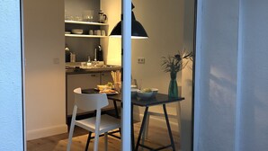 A compact kitchen with a dining area, featuring a white chair, a small table, and a vase with flowers. - Sunny, quiet city apartment with sleeping gallery and small private courtyard (Köln)