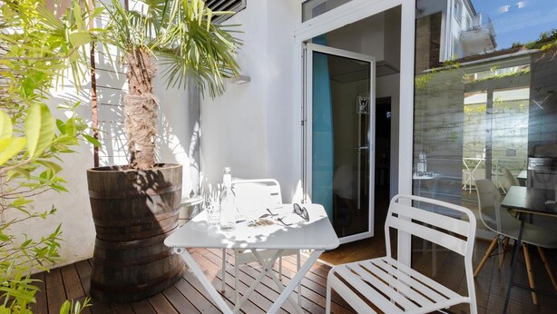 A patio with a white table and chair, a wooden barrel planter, and a sliding glass door leading to an outdoor area. - Sunny, quiet city apartment with sleeping gallery and small private courtyard (Köln)