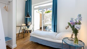 A bedroom with a bed, a desk, a chair, a small table with a lamp, and a window with curtains. - Sunny, quiet city apartment with sleeping gallery and small private courtyard (Köln)