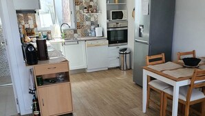 Une cuisine compacte avec des meubles blancs, un four à micro-ondes, un réfrigérateur et une table à manger avec des chaises.