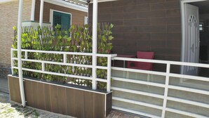 Un balcon doté d’une balustrade en métal blanc, d’une clôture en bois et d’une chaise rouge.