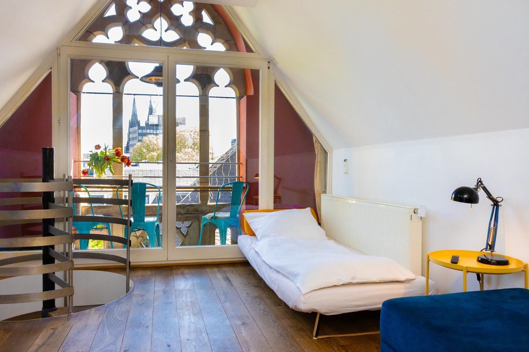 Ein Zimmer mit einem Bett, einem Tisch mit Stühlen, einem Heizkörper und einem Fenster mit Blick auf eine Stadtlandschaft.