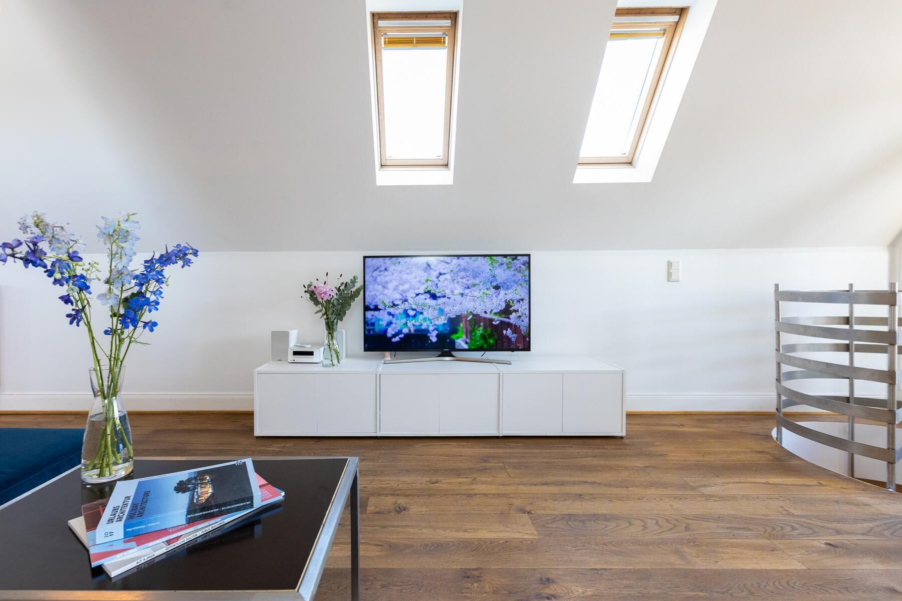 Un salon moderne doté d’un téléviseur à écran plat, d’un meuble de rangement blanc, d’un plancher en bois et de lucarnes.
