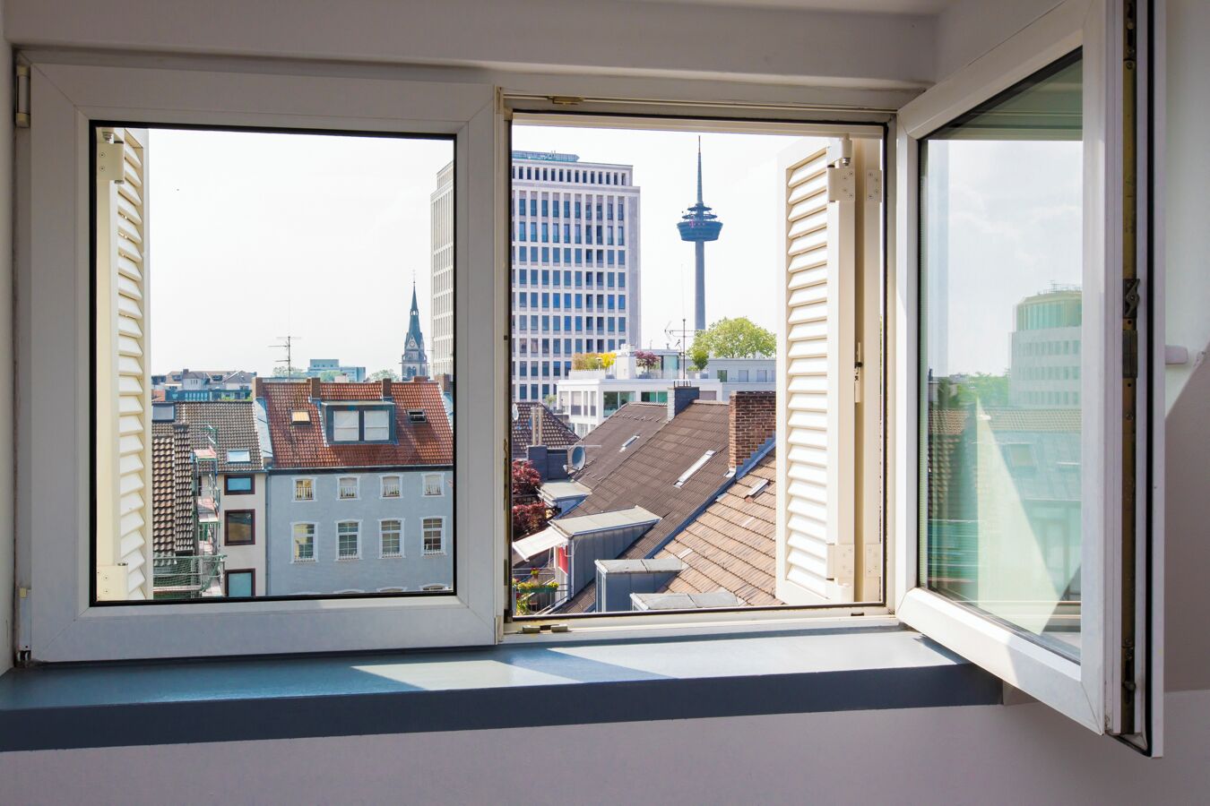 Ein Fenster mit Blick auf eine Stadtlandschaft, darunter ein Turm und verschiedene Gebäude.