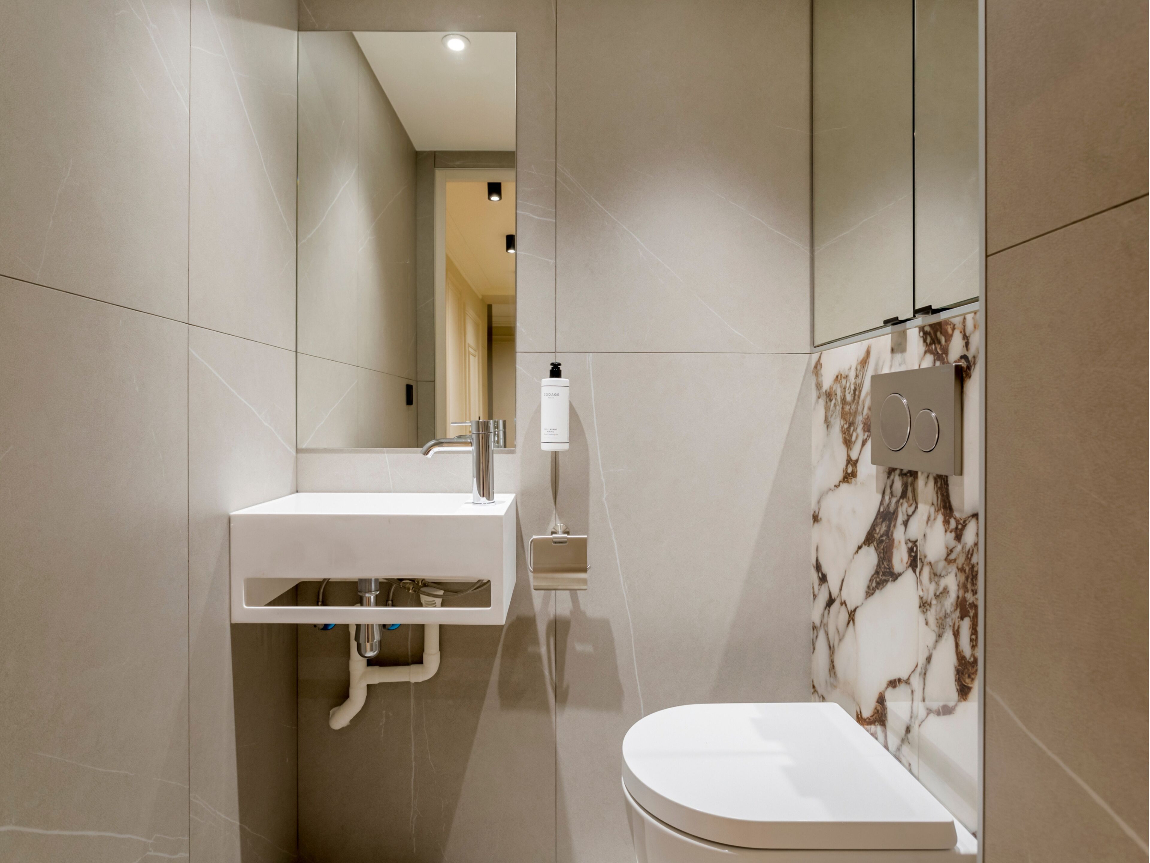A modern bathroom with a white sink, a mirror, and a toilet.