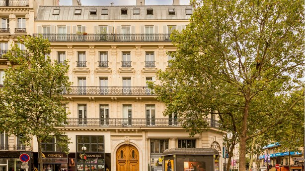 A multi-story building with a central entrance, a kiosk on the ground floor, and a visible storefront for a cosmetics store. - Merveil Luxury Suite - Bvd Saint Denis (Paris)