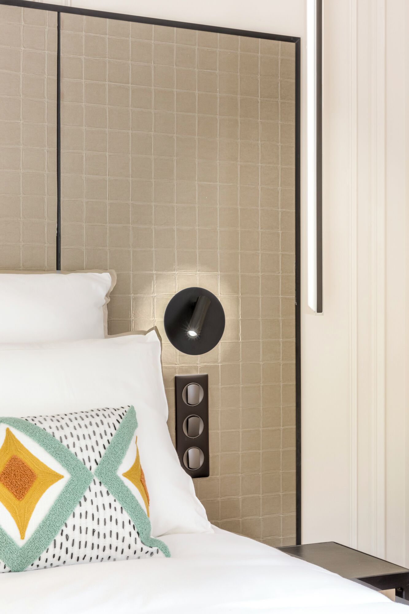 Quarto de hotel com uma cama, luminária fixada na parede e painel de controle.