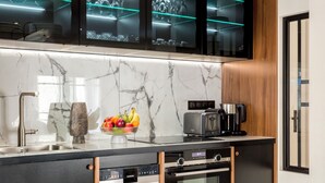 A modern kitchen with a marble countertop, black cabinetry, and a built-in oven. There is a fruit bowl on the counter and a coffee maker. - Merveil Luxury Suite - Bvd Saint Denis (Paris)