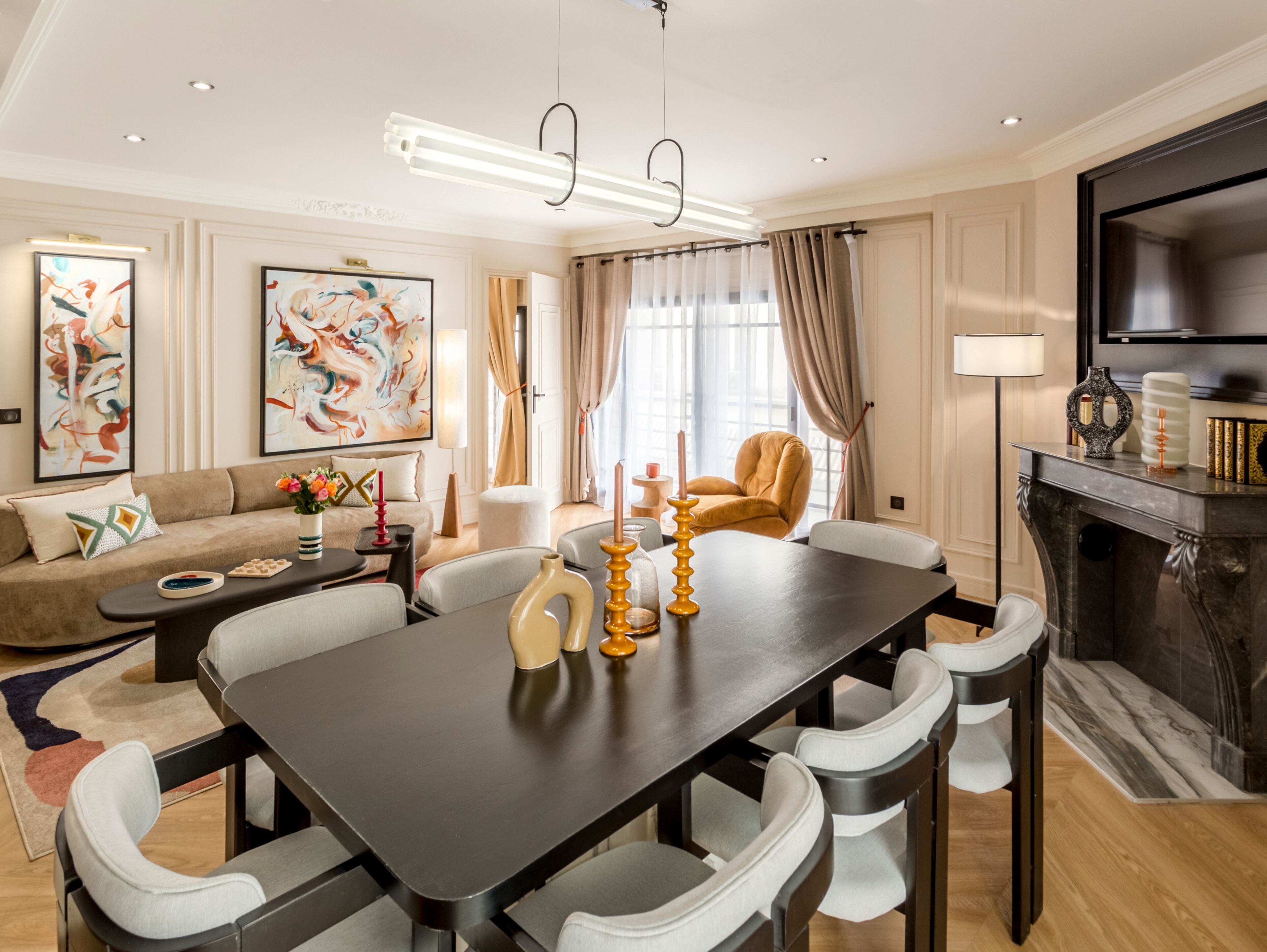 Una sala de estar moderna con una mesa de comedor de madera oscura, sillas tapizadas en blanco, un sofá color beige y arte abstracto en las paredes.