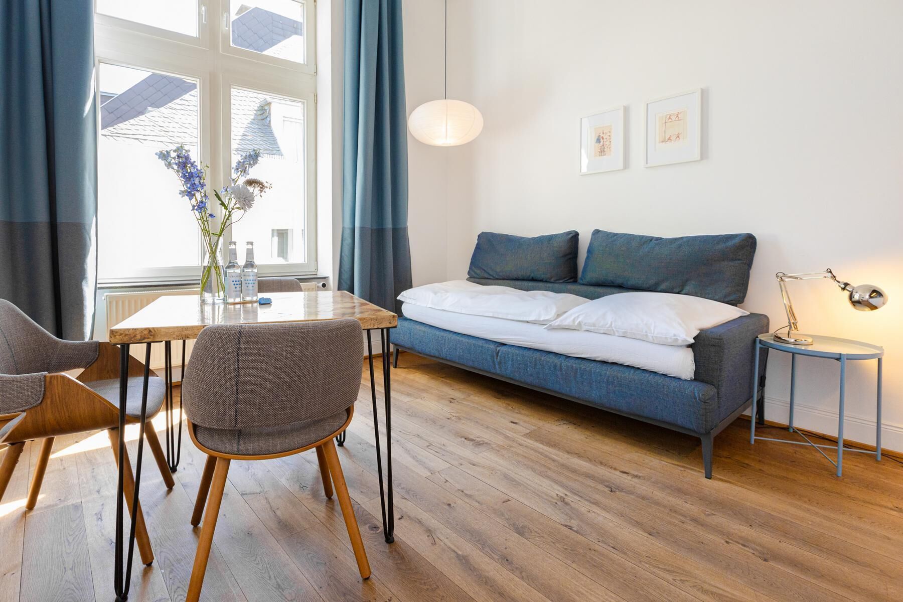 Ein modernes Zimmer mit einer Couch, einem Esstisch, Stühlen, einer Lampe und Kunstwerken an der Wand.