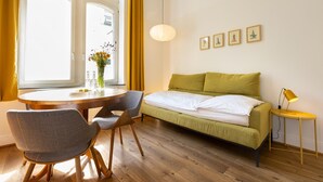 A room with a bed, a round table, a chair, a lamp, and a window with curtains.