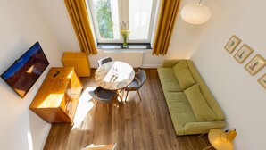 A modern living room with a wooden floor, a green sofa, a dining table with chairs, a TV, and a staircase.
