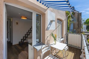 Een balkon met een witte tafel en stoelen, een blauw-wit gestreepte luifel en een houten terras.