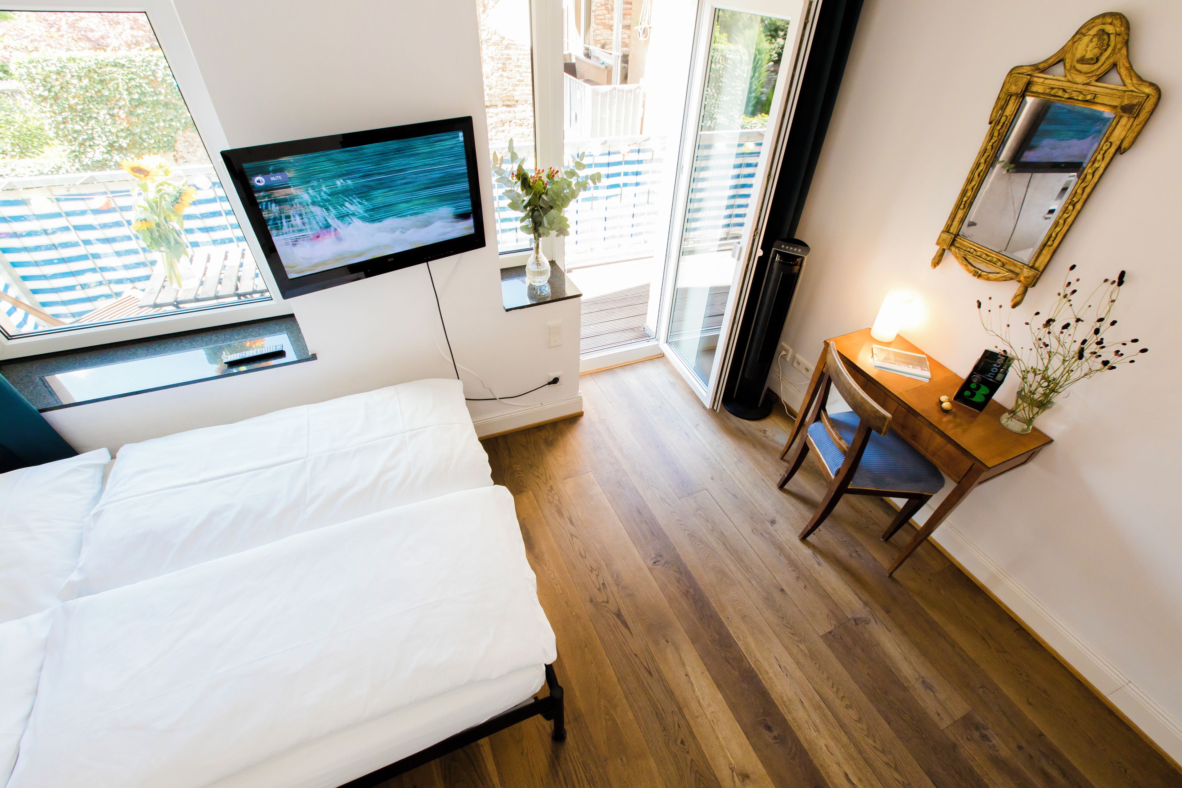 Ein Hotelzimmer mit einem Bett, einem Schreibtisch mit Lampe, einem Fernseher und einem Fenster mit Blick auf Grünflächen.