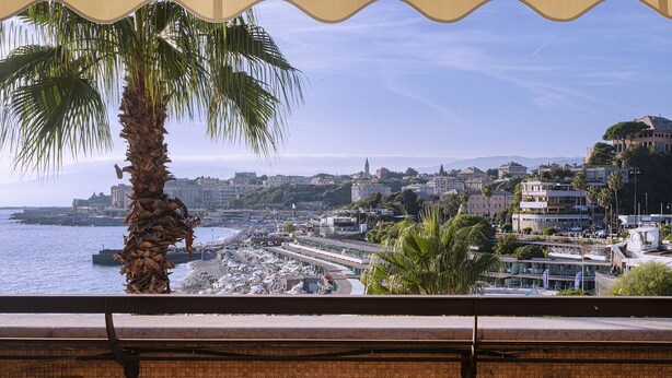 A coastal cityscape with buildings, a beach, and a palm tree. - Beachfront Studio With Terrace by Wonderful Italy (Genoa)