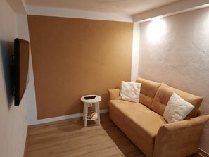 Ein Zimmer mit einer braunen Wand, einem beigen Sofa mit Kissen, einem kleinen weißen Beistelltisch und einem schwarzen Gegenstand auf dem Tisch.