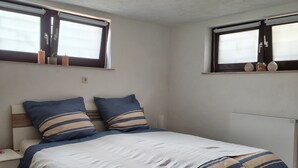 Une chambre à coucher avec un lit, une table de chevet et deux fenêtres équipées de stores.
