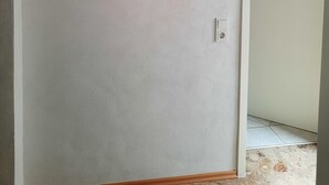 Une pièce avec un mur blanc, un tableau encadré représentant des fleurs séchées, un interrupteur et une porte donnant sur une autre pièce.