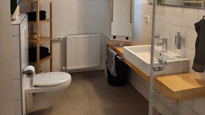 Une salle de bain moderne équipée de toilettes, d’un lavabo et d’une douche. Il y a une fenêtre au-dessus des toilettes et un miroir au-dessus du lavabo.