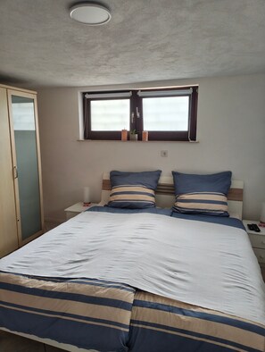 Ein Schlafzimmer mit Bett, Nachttisch, Fenster und Tür.