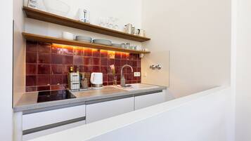 A modern kitchen with a red-tiled backsplash, stainless steel appliances, and wooden shelves above the counter.