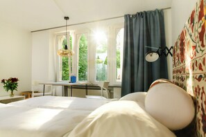 Une chambre à coucher avec un lit, un bureau et une chaise. Il y a une fenêtre avec des rideaux, un radiateur et un mur orné d’un motif.