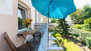 Un balcon avec un parasol bleu, une table en bois et une chaise. Un vase rempli de tournesols est posé sur la table.