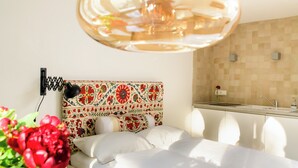 A hotel room with a bed, a decorative headboard, a small kitchenette, and a potted plant. - my.statthaus - 8 apartments exclusively for up to 22 people (Köln)