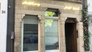 L’entrée d’un hôtel, avec une porte en verre, un panneau lumineux au-dessus et une porte en bois sur la droite.