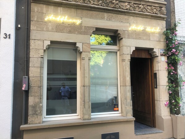 L’entrée d’un hôtel, avec une porte en verre, un panneau lumineux au-dessus et une porte en bois sur la droite.